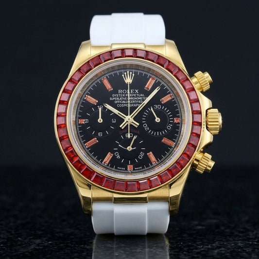 Gold-tone chronograph with a red baguette-stone bezel and a black dial on a white rubber strap, upright on polished black granite