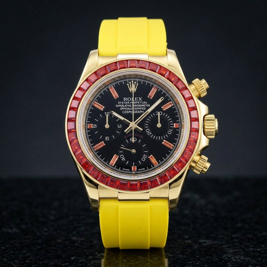 Gold-tone chronograph with a red baguette-stone bezel and a black dial on a bright yellow rubber strap, upright on polished black granite