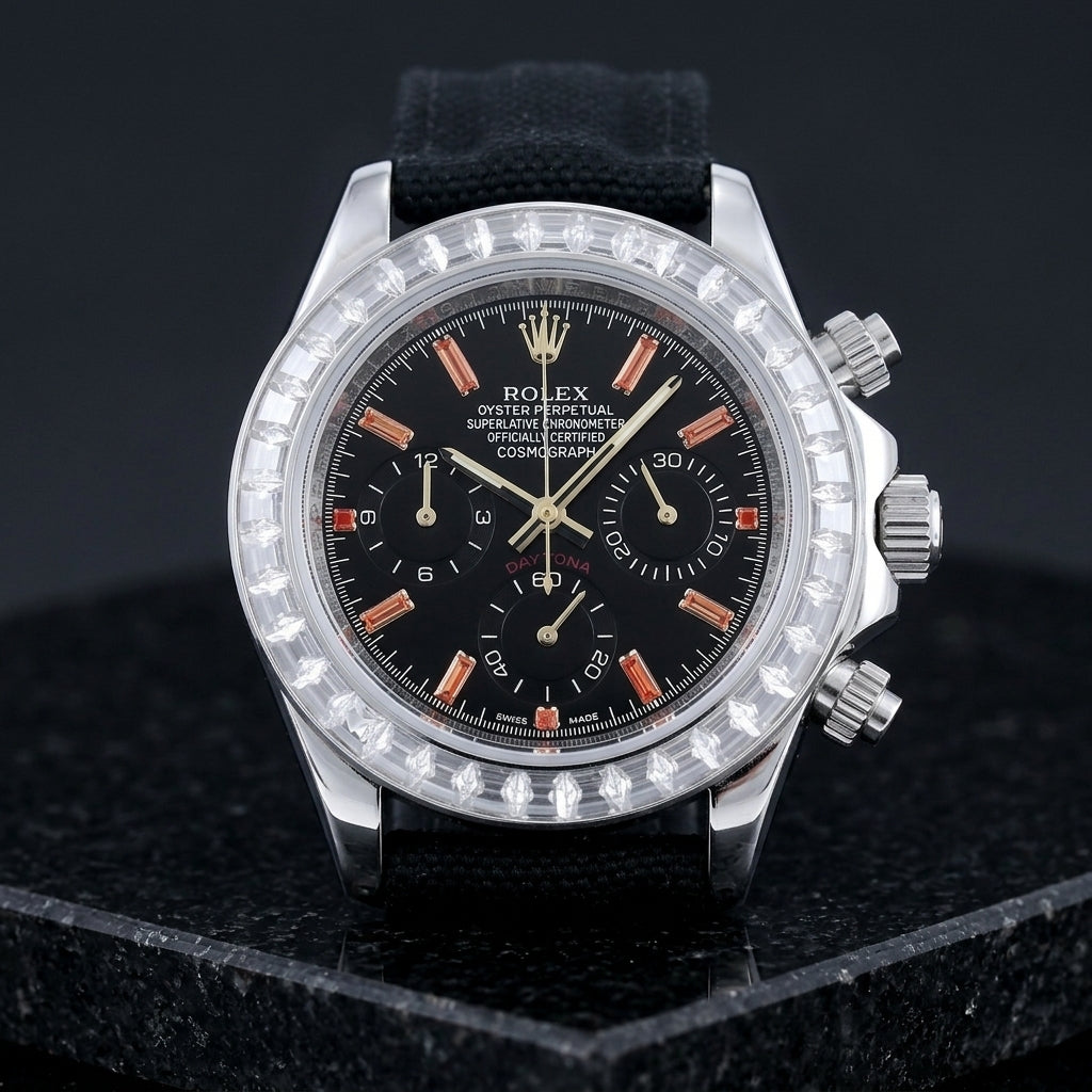 Steel chronograph with a black dial, orange stone markers and a clear baguette-stone bezel, upright on polished black granite