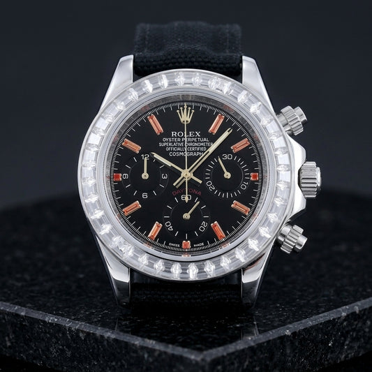 Steel chronograph with a black dial, orange stone markers and a clear baguette-stone bezel, upright on polished black granite