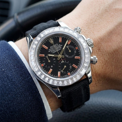 Steel chronograph with a black dial on its black canvas strap, worn on the wrist below a dark suit cuff