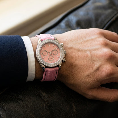 Steel chronograph with a pink dial on its pink canvas strap, worn on the wrist below a dark suit cuff