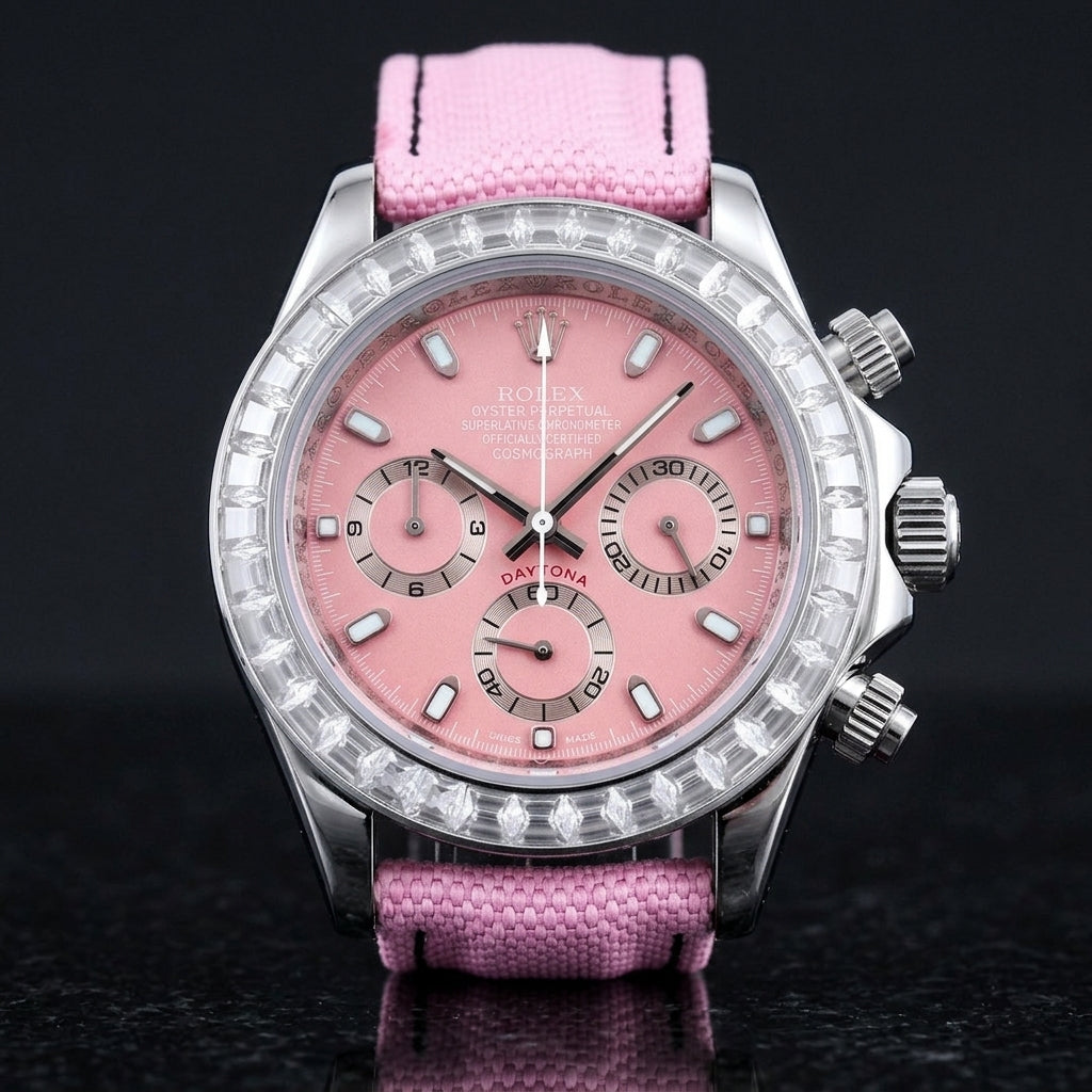 Steel chronograph with a pink dial on its pink canvas strap, worn on the wrist below a dark suit cuff