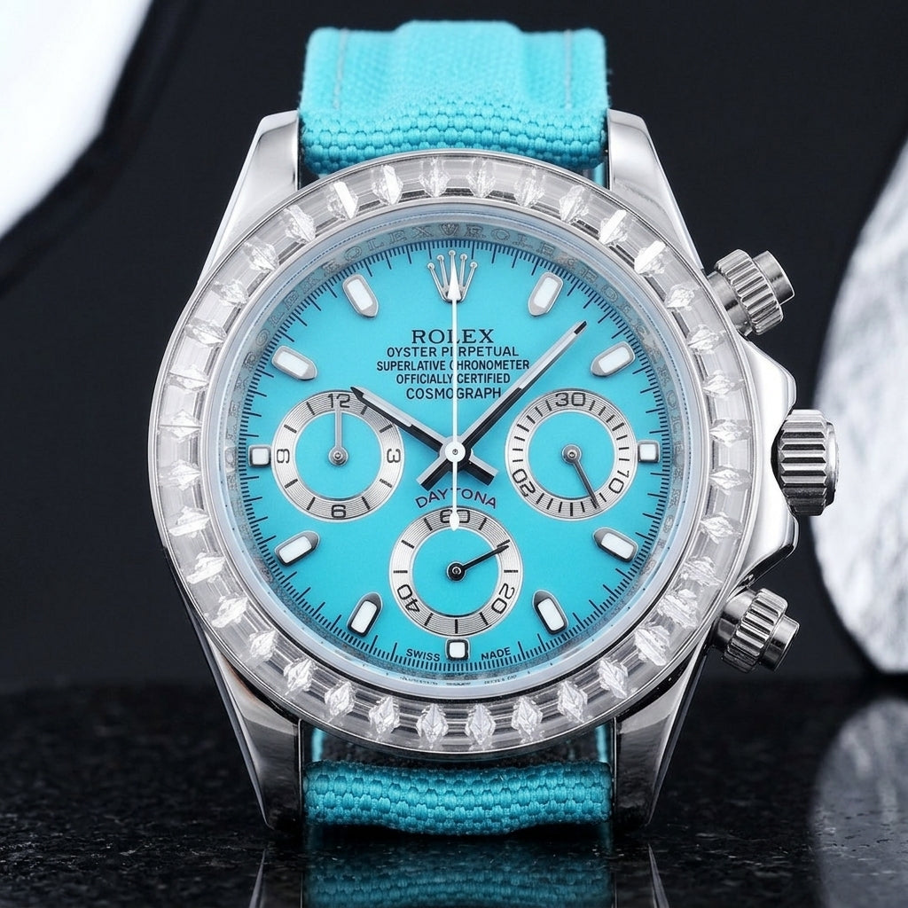 Steel chronograph with a turquoise dial on its turquoise canvas strap, worn on the wrist below a dark suit cuff