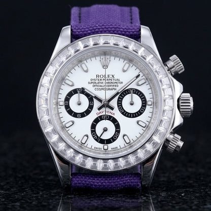 Steel chronograph with a white dial on its purple canvas strap, worn on the wrist below a dark suit cuff