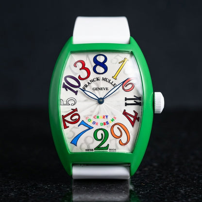 Green curved tonneau watch with a silver-white dial and multicoloured numerals out of order, upright on polished black granite