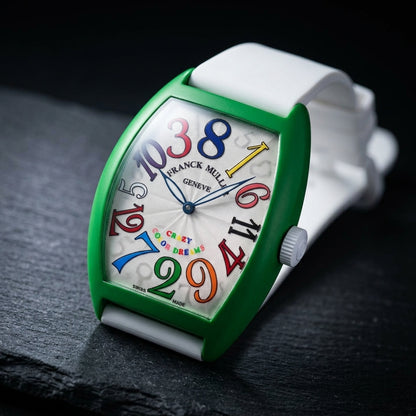 Green curved tonneau watch at a three-quarter angle on dark slate, its white fluted crown on the matte green flank
