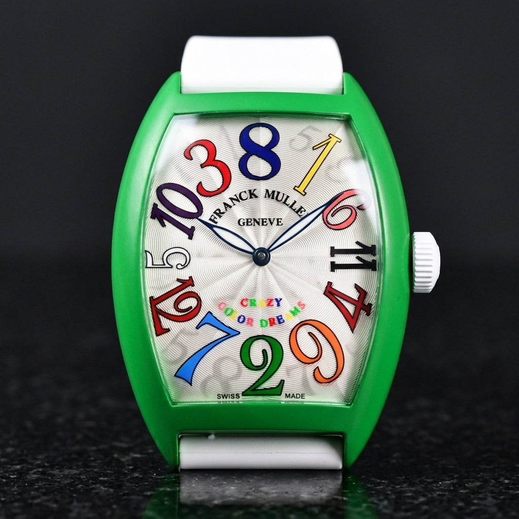 Green curved tonneau watch with rainbow numerals on its white rubber strap, worn on the wrist below a dark suit cuff