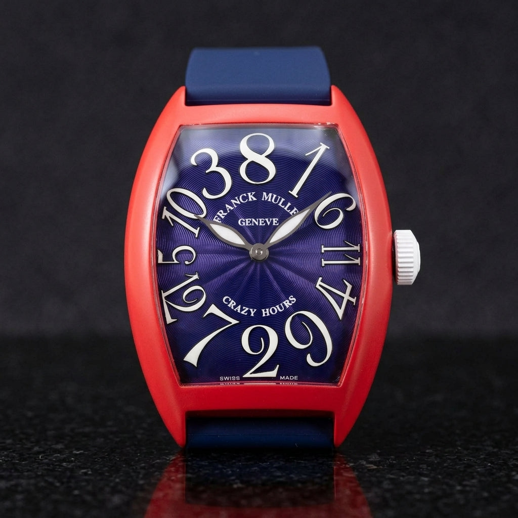 Red curved tonneau watch on its navy rubber strap, worn on the wrist below a dark suit cuff