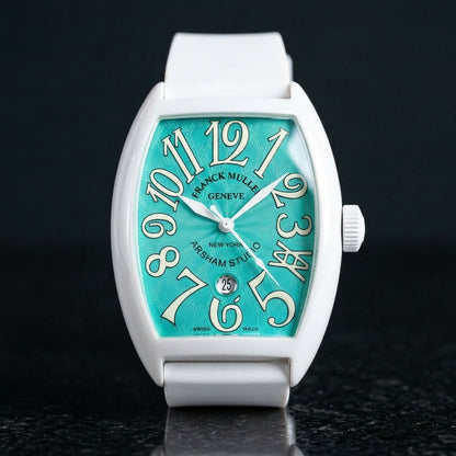 White curved tonneau watch with a turquoise dial and cream-white numerals, upright on polished black granite