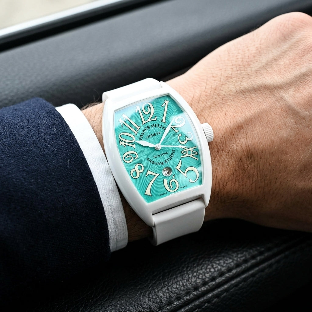 White curved tonneau watch with a turquoise dial on its white rubber strap, worn on the wrist below a dark suit cuff