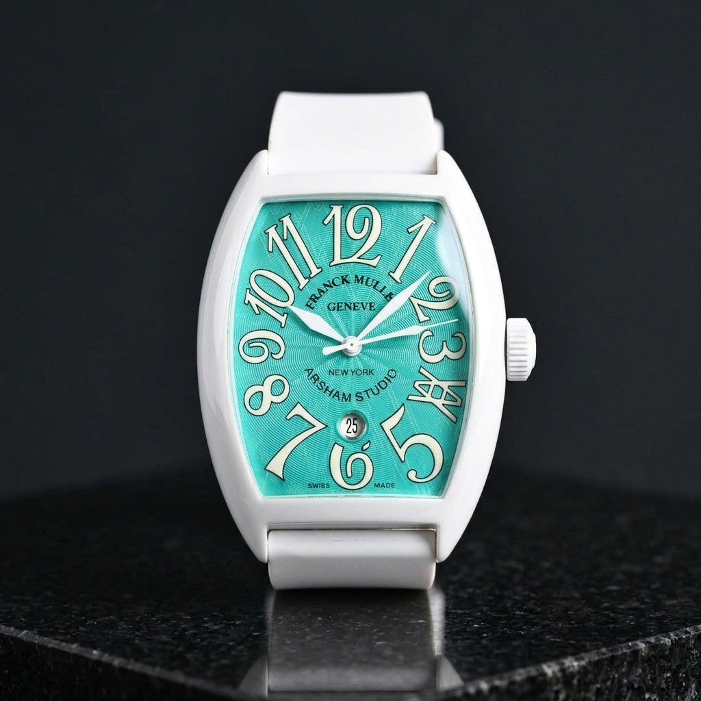 White curved tonneau watch with a turquoise dial on its white rubber strap, worn on the wrist below a dark suit cuff