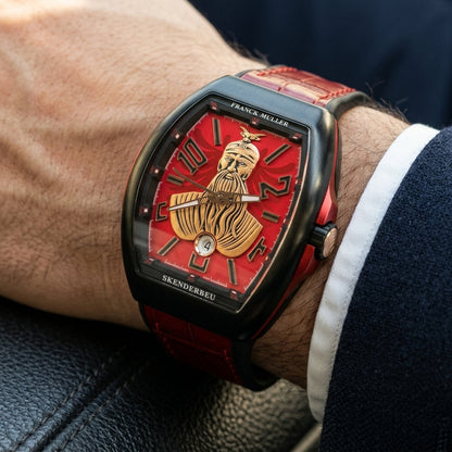 Black curved tonneau watch with a red dial on its red strap, worn on the wrist below a dark suit cuff