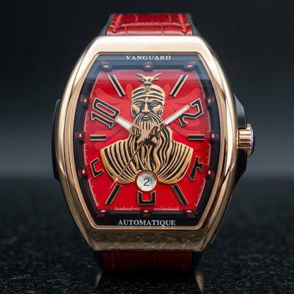 Rose gold curved tonneau watch with a red dial and a raised gold-tone warrior portrait, upright on polished black granite