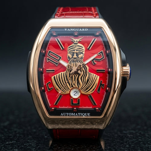 Rose gold curved tonneau watch with a red dial and a raised gold-tone warrior portrait, upright on polished black granite