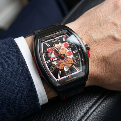 Black curved tonneau watch on its black crocodile-pattern strap with red stitching, worn on the wrist below a dark suit cuff