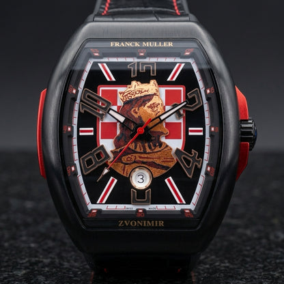 Black curved tonneau watch on its black crocodile-pattern strap with red stitching, worn on the wrist below a dark suit cuff