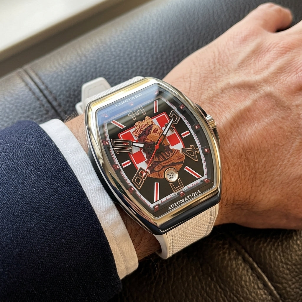 Steel curved tonneau watch on its white strap, worn on the wrist below a dark suit cuff