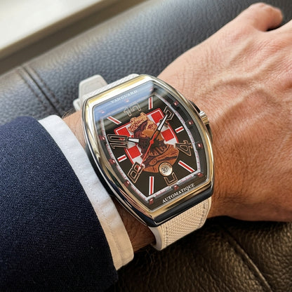 Steel curved tonneau watch on its white strap, worn on the wrist below a dark suit cuff