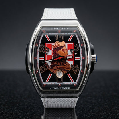 Steel curved tonneau watch on its white strap, worn on the wrist below a dark suit cuff