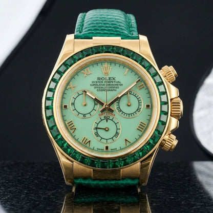 Gold-tone chronograph with a pale green dial and a green stone bezel on a green lizard-grain strap, worn on the wrist below a navy suit cuff