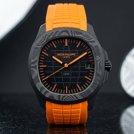 Black forged-carbon grid-dial watch with orange batons and a bright orange rubber strap, upright on polished black granite