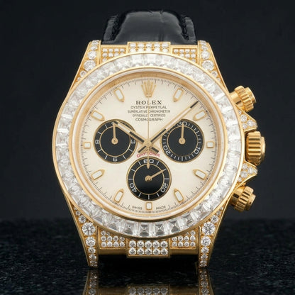 Gold chronograph with an ivory and black dial and a clear stone bezel on a black alligator strap, worn on the wrist below a navy suit cuff