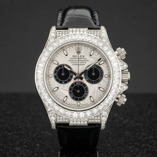 White gold-wrapped chronograph with a silver-grey meteorite dial, three black counters and a clear baguette bezel standing upright on polished black granite