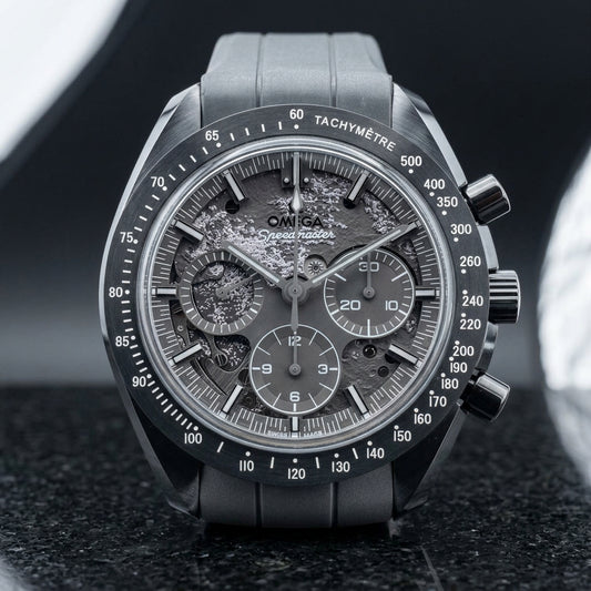 Grey ceramic chronograph with a mid-grey moon relief dial and all-grey hands, standing upright on polished black granite