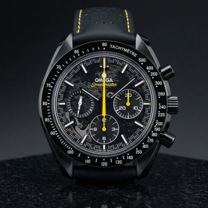Black ceramic chronograph with a black moon relief dial and a yellow chronograph hand, standing upright on polished black granite