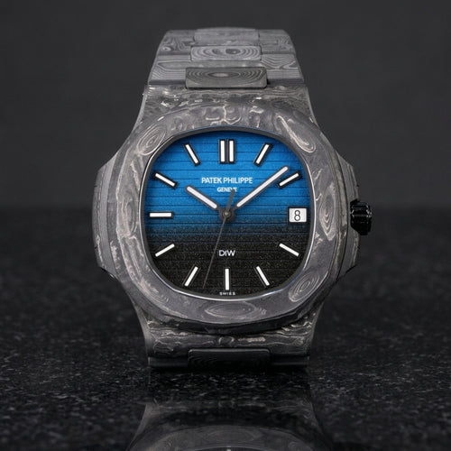 Forged carbon sports watch with a blue-to-black gradient dial and white baton markers, upright on polished black granite