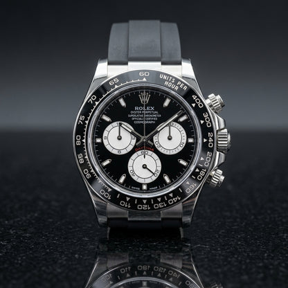 Steel chronograph with a black dial and white counters on its black rubber strap, worn on the wrist below a dark suit cuff
