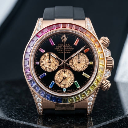 Rose-gold chronograph with a rainbow baguette-stone bezel and a black dial with rainbow markers, upright on polished black granite