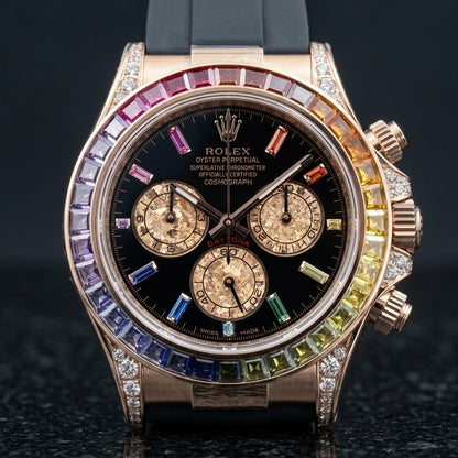 Rose-gold chronograph with a rainbow stone bezel on its black rubber strap, worn on the wrist below a dark suit cuff