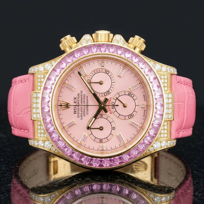 Gold chronograph with a pink dial and a pink stone bezel on a pink alligator strap, worn on the wrist below a navy suit cuff