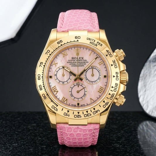 Gold-tone chronograph with a pink mother-of-pearl dial, gold Roman numerals and an engraved tachymeter bezel standing upright on polished black granite