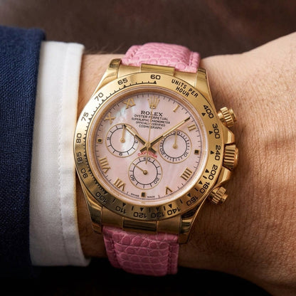 Gold-tone chronograph with a pink mother-of-pearl dial on a pink lizard-grain strap, worn on the wrist below a navy suit cuff