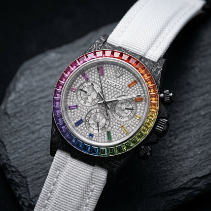Black forged carbon chronograph at a three-quarter angle on dark slate, its black crown and pushers beside the rainbow bezel