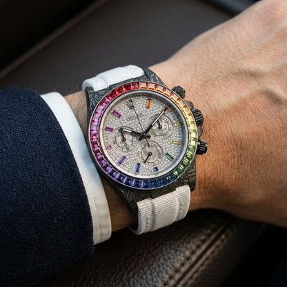 Rainbow-bezel carbon chronograph on its white woven strap, worn on the wrist below a navy suit cuff