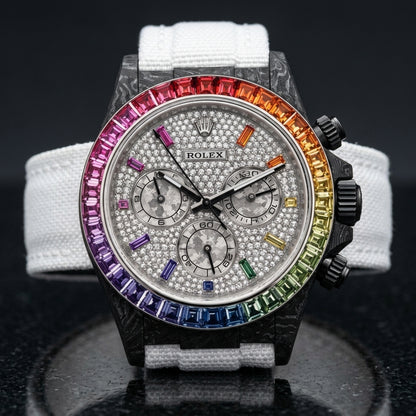 Rainbow-bezel carbon chronograph on its white woven strap, worn on the wrist below a navy suit cuff