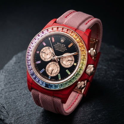 Red carbon chronograph at a three-quarter angle on dark slate, its rose-gold crown and pushers beside the rainbow bezel
