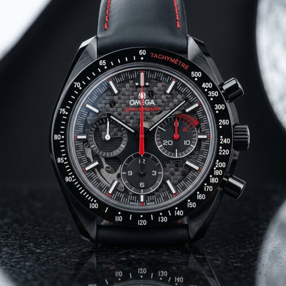 Black ceramic chronograph on a black perforated strap with red stitching, worn on a wrist below a navy suit cuff