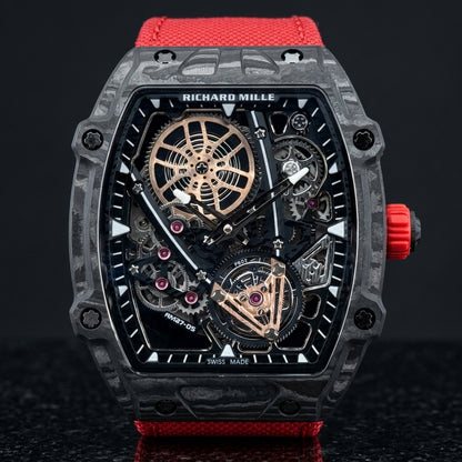 Black carbon skeleton tonneau watch on its red woven strap, worn on the wrist below a dark suit cuff
