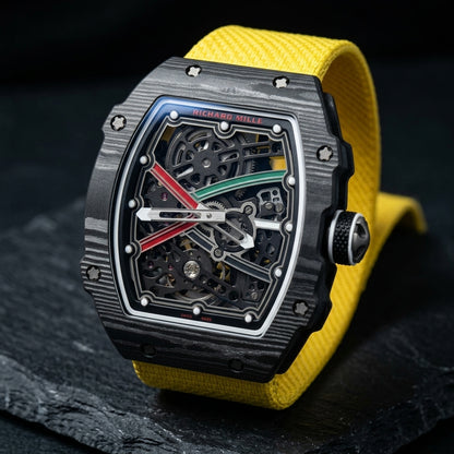 Black carbon tonneau watch at a three-quarter angle on dark slate, grey layer waves across the case and a black dimpled crown with a grey cross end