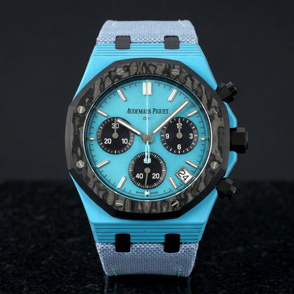 Octagonal chronograph with a sky-blue case on its light-blue canvas strap, worn on the wrist below a dark suit cuff