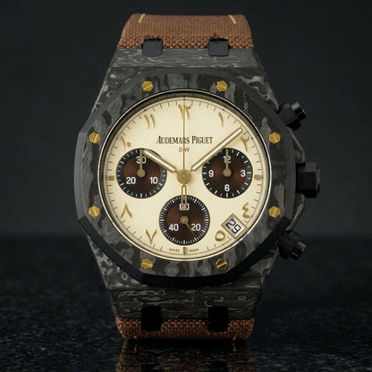 Black forged-carbon octagonal chronograph with a cream dial and gold Eastern Arabic numerals, upright on polished black granite