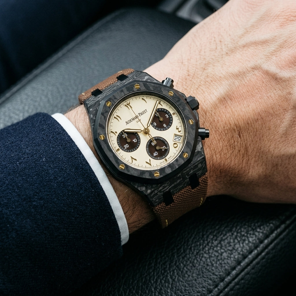 Black forged-carbon octagonal chronograph with a cream dial on its brown canvas strap, worn on the wrist below a dark suit cuff