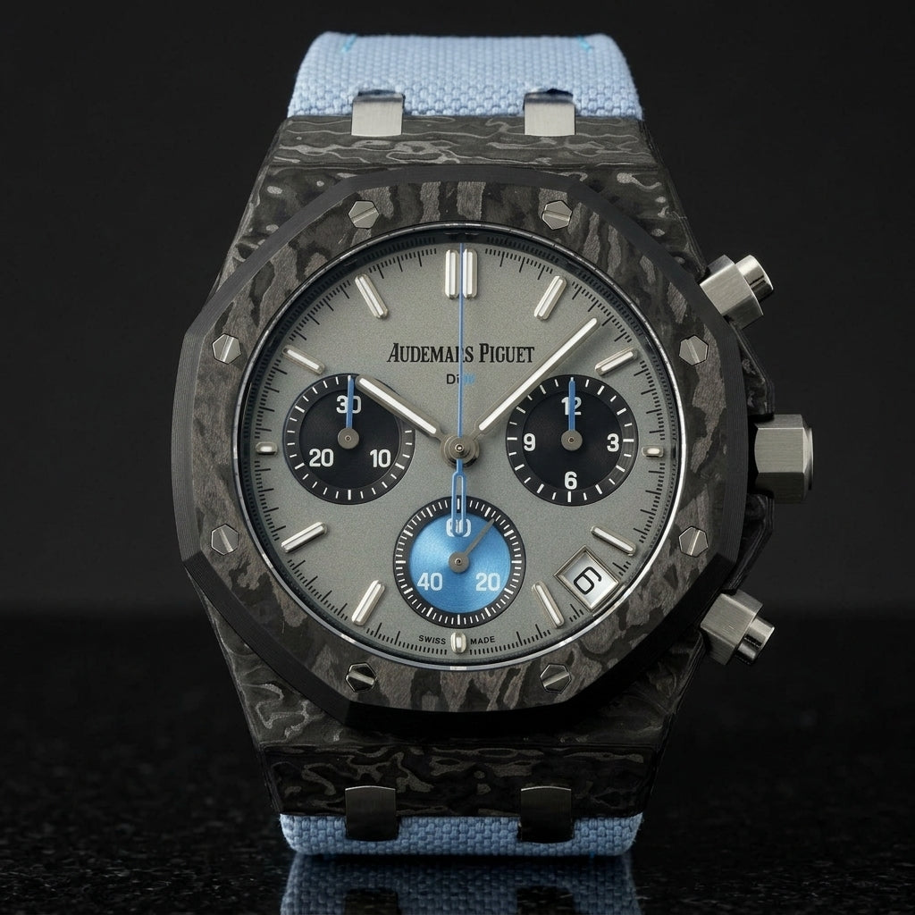 Black forged-carbon octagonal chronograph with a grey dial and a sky-blue counter, upright on polished black granite