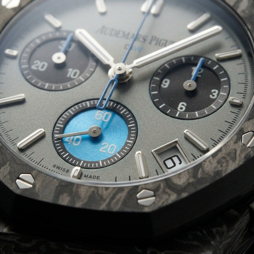 Macro of the grey dial with steel batons, two black counters and the sky-blue counter at six inside the octagonal carbon bezel