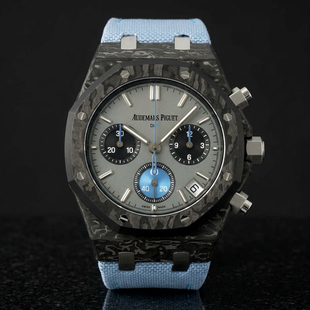 Black forged-carbon octagonal chronograph on its light-blue canvas strap, worn on the wrist below a dark suit cuff